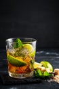 Whiskey and Cola cocktail with lime, mint and ice, alcoholic drink in a glass on a dark wooden background