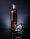 Whiskey with ice cubes in glass near bottle on black background, cold atmosphere Royalty Free Stock Photo