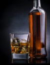 Whiskey with ice cubes in glass near bottle on black background, cold atmosphere Royalty Free Stock Photo