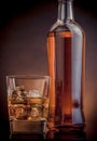 Whiskey with ice cubes in glass near bottle on black background, warm atmosphere Royalty Free Stock Photo