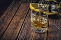 Whiskey is pouring from a bottle into a stack on a wooden surface.