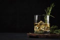 Whiskey, scotch or bourbon glass with fresh rosemary, ice cubes on black background