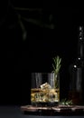 Whiskey, scotch or bourbon glass with fresh rosemary, ice cubes on black background