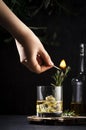 Whiskey, scotch or bourbon glass with fresh rosemary, ice cubes on black background. Bartender sets fire with match, fire burns