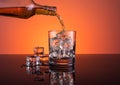 Whisky alcohol pouring into glass with ice drink on orange background Royalty Free Stock Photo