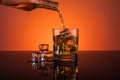 Whisky alcohol pouring into glass with ice drink on orange background Royalty Free Stock Photo