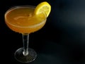 A whisky sour in a coupe glass with a lemon wagon wheel garnish with a dark background