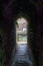 View down dark stone arched passageway through historic wall with view on other side of old seaside town Royalty Free Stock Photo