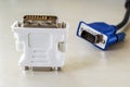 White adapter for connecting dvi-d and vga and blue monitor cord behind it. Connection of computer devices with plugs of different