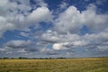 White air clouds in the bright blue sky above the field of mown wheat Royalty Free Stock Photo