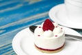 White airy cake with raspberry layer and raspberry berry lies on a white round plate next to a white cup, which stands on a blue Royalty Free Stock Photo