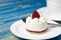 White airy cake with raspberry layer and raspberry berry lies on a white round plate next to a white cup, which stands on a blue