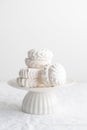 White airy zephyr or marshmallow shells on a white cake stand on a white table, space for text