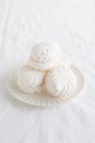 White airy zephyr or marshmallow shells on a plate on a white table, with space for text