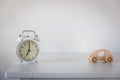 alarm clock with arrows at seven o`clock in the morning. Small wooden car in Scandinavian style on a white chest of drawers