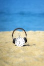 White alarm clock with brown headphones placed on the sand. Beautiful blue sea and sky as a background. Concept for relaxation, tr