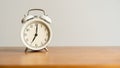 White alarm clock on brown wood desk and cream wallpaper textured background with copy space