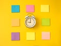 White alarm clock and colorful sticky notes on a yellow background. The concept of working time. Workplace Royalty Free Stock Photo