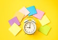 White alarm clock and colorful sticky notes on a yellow background. The concept of working time. Workplace Royalty Free Stock Photo