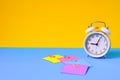 White alarm clock and colorful sticky notes on a yellow blue background. The concept of working time. Workplace Royalty Free Stock Photo