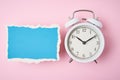 White alarm clock and empty torn paper sheet on a pink background, top view. Time concept Royalty Free Stock Photo