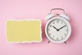 White alarm clock and empty torn paper sheet on a pink background, top view. Time concept Royalty Free Stock Photo