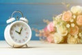 White alarm clock and flowers pink and red rose on wooden table and blue background with copy space for add text and content