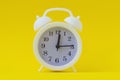 White alarm clock 12 hours 15 minutes. Bright yellow background, copy space