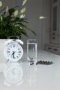 White alarm clock and medical pills with a glass of water on the table. Healthcare and medicine. Vitamins and mineral supplements Royalty Free Stock Photo