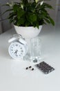 White alarm clock and medical pills with a glass of water on the table. Healthcare and medicine. Vitamins and mineral supplements Royalty Free Stock Photo