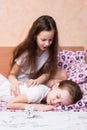 White alarm clock stands on the table on the background of a girl trying to wake up another girl Royalty Free Stock Photo