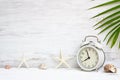 White alarm clock with starfish, sea shells and green palm leaf background. Background concept for Summer time holiday vacation. Royalty Free Stock Photo