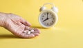 White alarm clock, tablets on a yellow background. Hand of a woman taking pills. Concept of healthcare and medicin