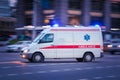 White Ambulance Van crosses a wide city street. Emergency vehicle with warning lights and siren moving fast on an avenue