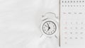 White analog alarm clock and calendar on white bed , travel schedule or work from home concept