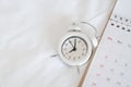 white alarm clock and calendar on white bed , lifestyle and planning , travel schedule or work from home concept