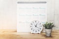 white analog clock with blurred white calendar and plant on desk