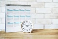 White analog clock with blurred calendar on wooden table