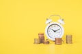 White analog clock white blurred stack of coins on vivid yellow background for business and finance concept