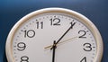 A detailed close-up of a white analog wall clock with black numerals and hands, set against a dark blue background showing the top Royalty Free Stock Photo