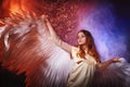 White angel on a dark background with colored lighting. The concept of war between good and evil. Girl with angel wings during a