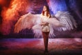 White angel on a dark background with colored lighting. The concept of war between good and evil. Girl with angel wings during a