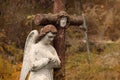 A white angel is praying. A statue stands next to an old cross (concept: religion) Royalty Free Stock Photo