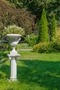 White antique ceramic vase with flowers on a column in a summer garden Royalty Free Stock Photo