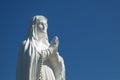 White antique statue of Virgin Mary praying against blue sky. Copy space Royalty Free Stock Photo