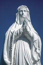 White antique statue of Virgin Mary praying against blue sky. Copy space. Vertival image