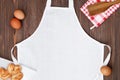 Blank white apron template on wooden table with cookies and eggs, copy space. Kitchen, cooking clothing mockup