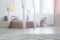 White armchair next to canopied bed in pink pastel bedroom inter