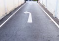 White arrow traffic sign indicates minor road to turn left to major road and white footpath lines on the asphalt rural road in