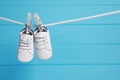 White baby shoes drying on washing line against light blue wooden wall. Space for text Royalty Free Stock Photo